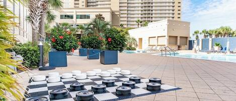 A pool area with a checkered pattern of tires and potted plants, a poolside lounge, and a tall building in the background.