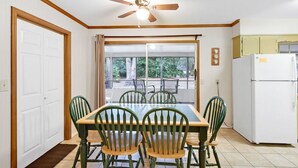 A dining area with a table and chairs, a ceiling fan, a refrigerator, and a view through a sliding glass door. - Carole Cottage - close to golf, tennis, and the beach (Jekyll Island)