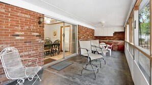 A covered patio with brick walls, a sliding glass door leading to a dining area, and a ceiling fan. - Carole Cottage - close to golf, tennis, and the beach (Jekyll Island)