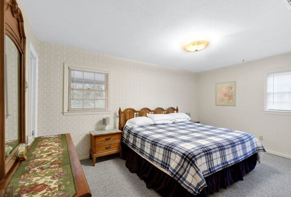 Une chambre à coucher comprenant un lit, une table de chevet, une commode, un miroir et une fenêtre avec des stores.