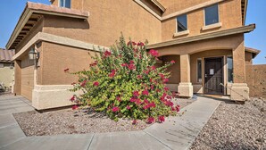 A two-story house with a stucco exterior, a front entrance with a door, and a small garden with pink flowers. - Maricopa Home w/ Outdoor Seating, 2 Mi to Golf! (Maricopa)