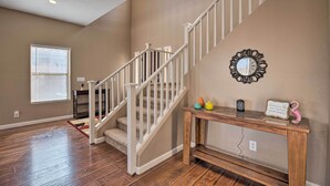 A staircase with white railings, a wooden console table with decorative items, and a wall-mounted mirror. - Maricopa Home w/ Outdoor Seating, 2 Mi to Golf! (Maricopa)