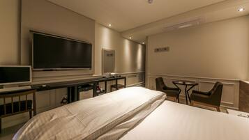 Une chambre d’hôtel équipée d’un lit, d’un bureau, d’une télévision et de deux chaises.