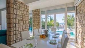 A dining area with a stone accent wall, a pool view, and a table set for four. - Villa Carpe Diem (Selce)