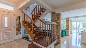 A spacious living area with a wooden staircase, a stone accent wall, and a view of the outdoors. - Villa Carpe Diem (Selce)