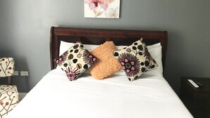A neatly made bed with floral-patterned pillows and a single fluffy pillow, a wooden headboard, and a wall-mounted artwork. - MODERN LUXURY 1BR/1BA/COZY/VIEWS OF KINGSTON (Kingston)