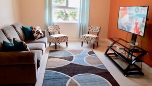A living room with a sofa, two patterned chairs, a coffee table, a TV, and a window with curtains. - MODERN LUXURY 1BR/1BA/COZY/VIEWS OF KINGSTON (Kingston)