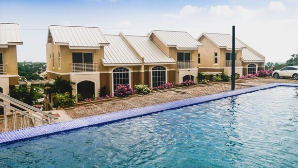 A swimming pool with a tiled edge, adjacent to a row of beige buildings with arched windows and a flat roof. - MODERN LUXURY 1BR/1BA/COZY/VIEWS OF KINGSTON (Kingston)