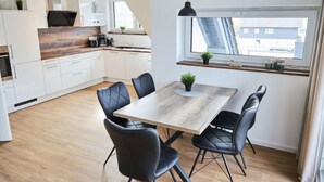 A modern kitchen with white cabinets, a wooden countertop, and a dining area with a wooden table and black chairs. - Landliebe by Interhome (Attendorn)