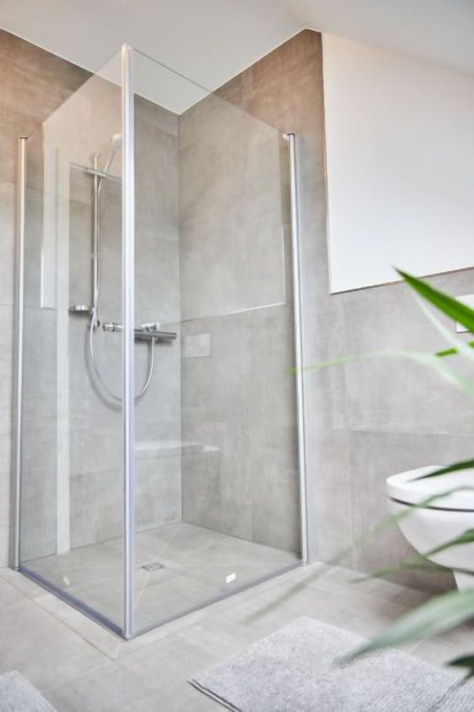 A modern bathroom with a glass-enclosed shower, a white toilet, and a marble floor.