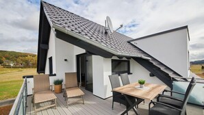 A modern house with a sloped roof, a balcony with a wooden deck, and a dining area with chairs and a table. - Landliebe by Interhome (Attendorn)