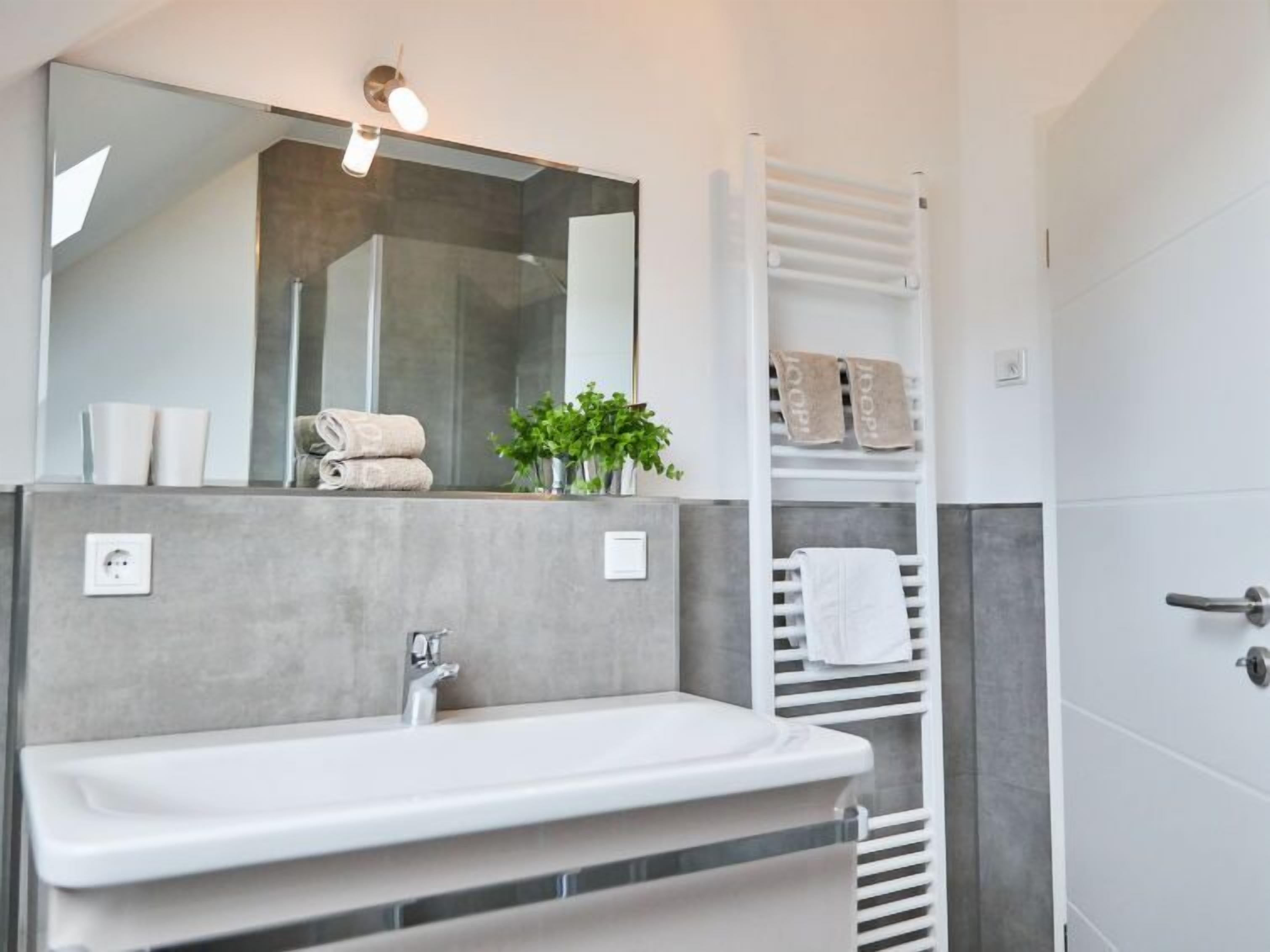 Ein modernes Badezimmer mit Waschbecken, Spiegel, Handtuchhalter und einer Duschkabine.