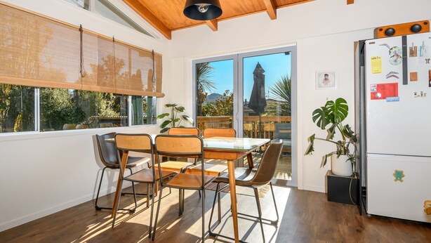 Une cuisine moderne avec une table à manger, des chaises, un réfrigérateur et de grandes fenêtres donnant sur un paysage de montagne et de verdure.
