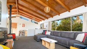 Un salon moderne avec un grand canapé d’angle gris, une table basse en bois et une cheminée. Une grande fenêtre offre une vue sur les arbres à l’extérieur.