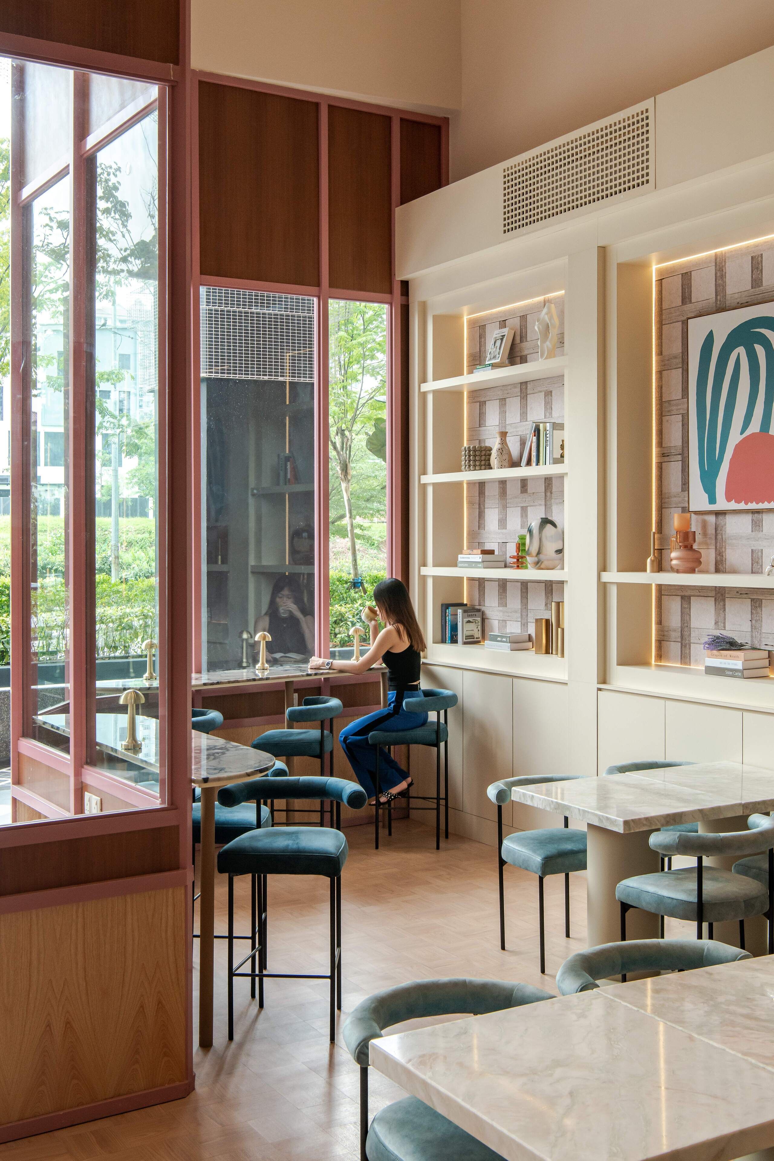 Een modern café met houten lambrisering, marmeren tafels en blauwe stoelen met kussens.