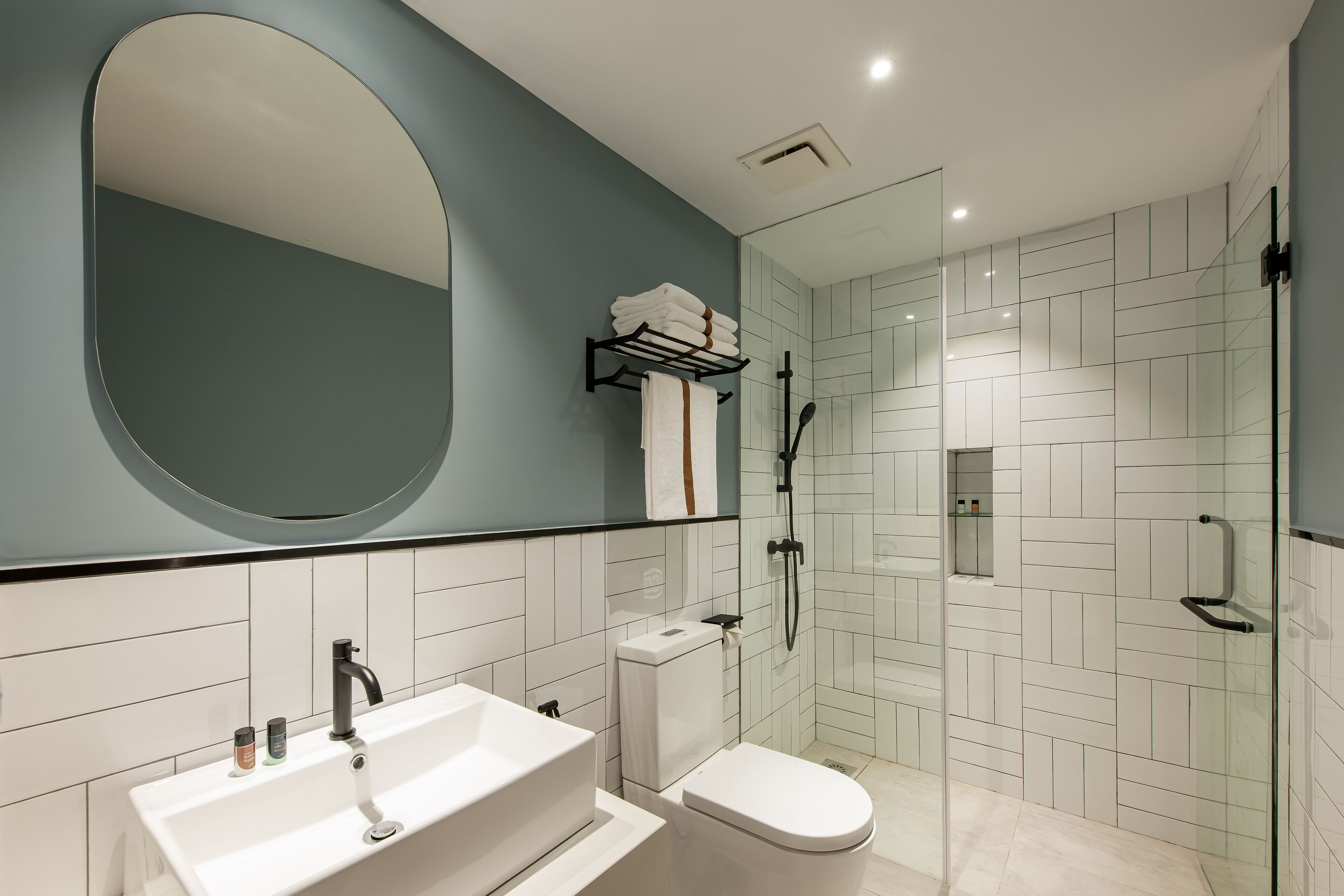 A modern bathroom with a large mirror, a white sink, a toilet, and a glass-enclosed shower area.