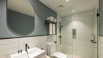 A modern bathroom with a large mirror, a white sink, a toilet, and a glass-enclosed shower area.