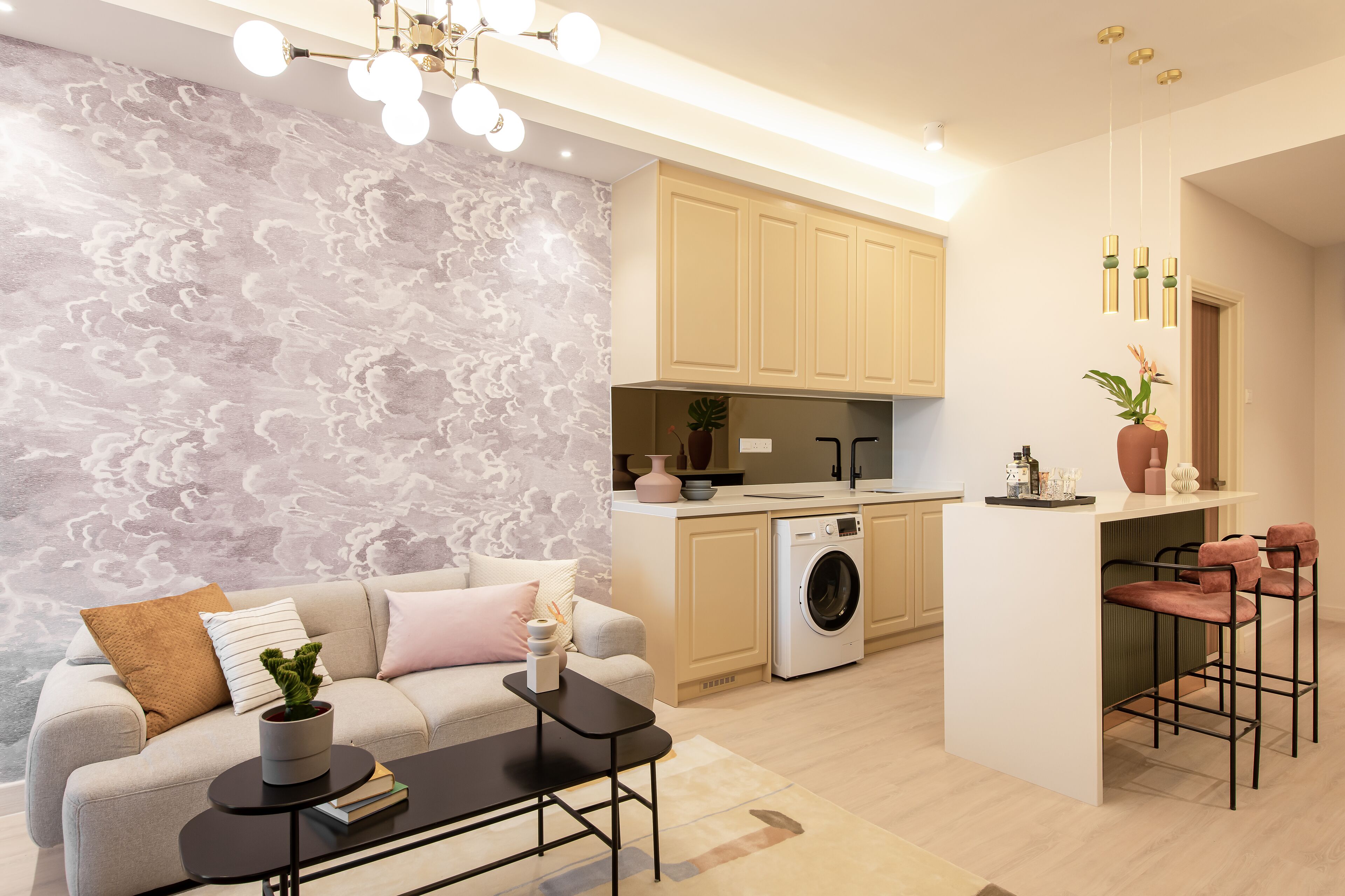 A modern kitchen with a washing machine, a bar area with two bar stools, and a sofa with a coffee table.