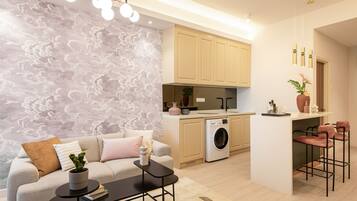 A modern kitchen with a washing machine, a bar area with two bar stools, and a sofa with a coffee table.