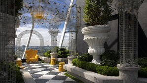 Un jardín en la azotea con piso a cuadros, plantas en macetas y una silla decorativa.