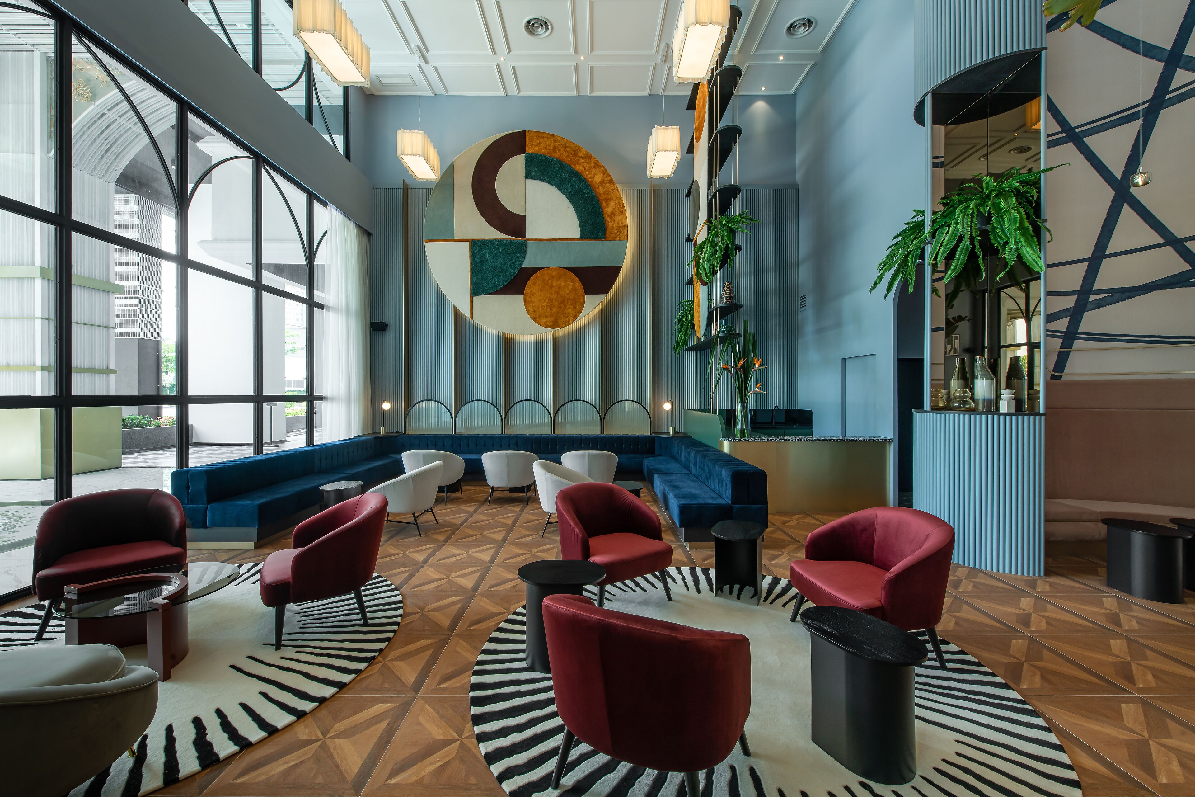 A modern lobby with a large abstract wall art, seating area with red and white chairs, and a blue sofa.