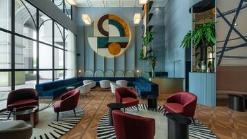 A modern lobby with a large abstract wall art, seating area with red and white chairs, and a blue sofa.