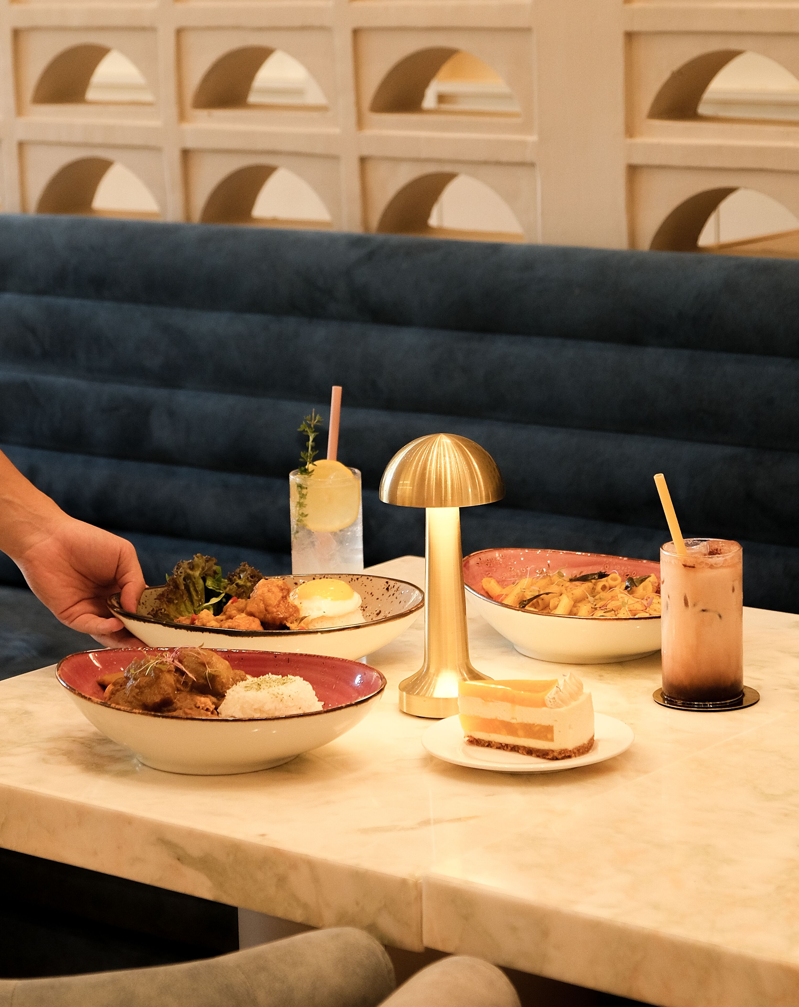 A dining table with various dishes, a decorative lamp, and a blue upholstered bench in the background.
