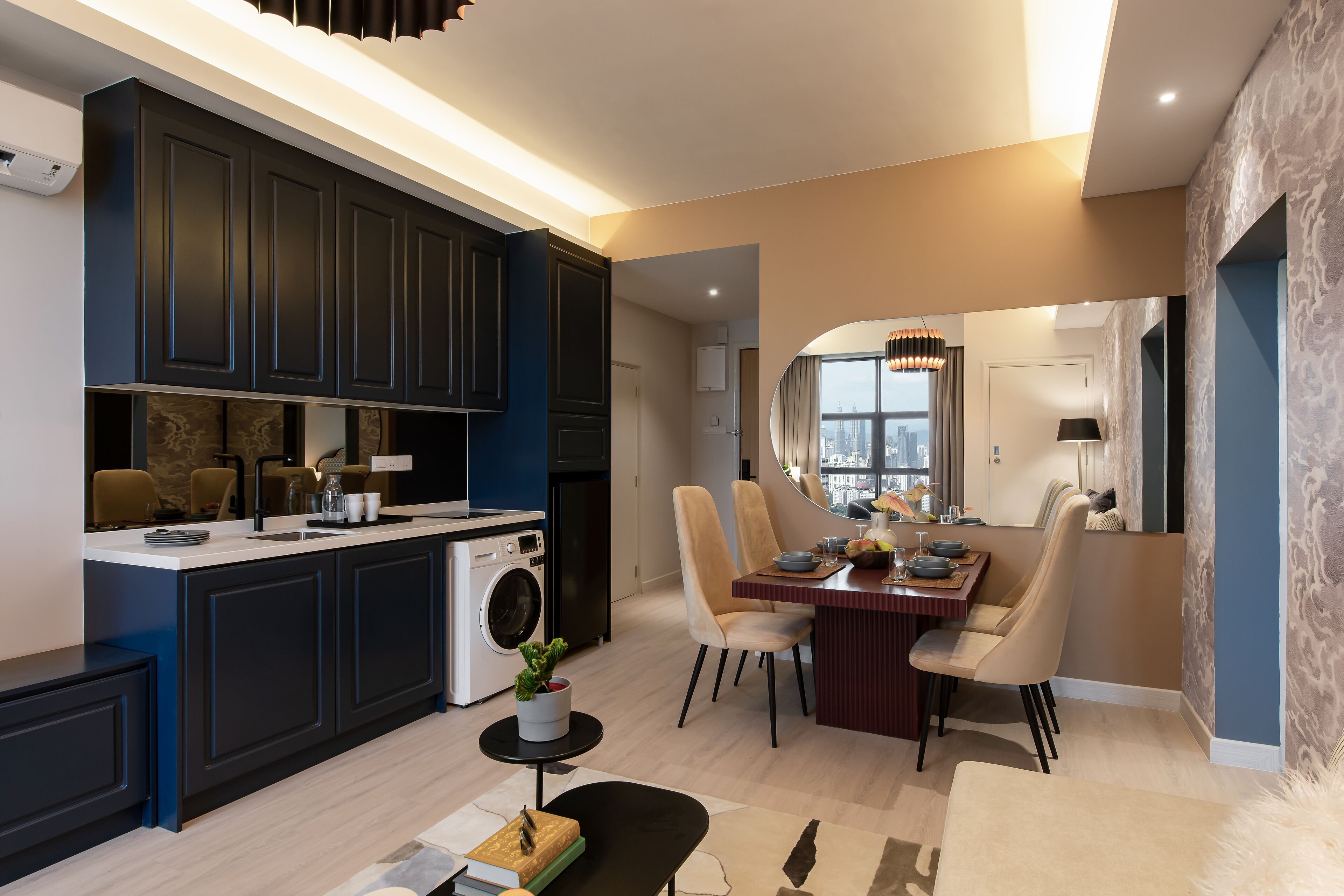 A modern kitchen with dark cabinetry, a dining area with a round table and chairs, and a view of the city through a large window.