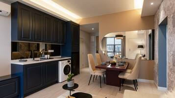 A modern kitchen with dark cabinetry, a dining area with a round table and chairs, and a view of the city through a large window.