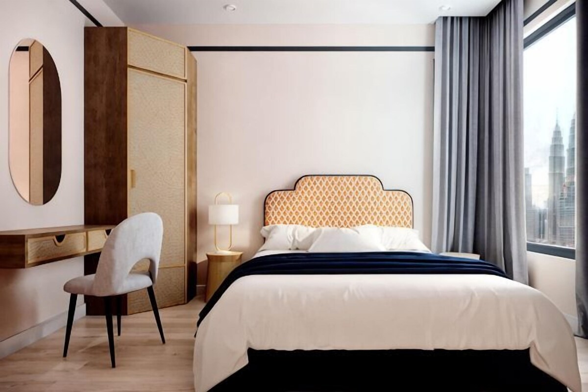 Una habitación de hotel moderna con cama, escritorio, silla, mesita de noche y un ventanal con vistas a la ciudad.