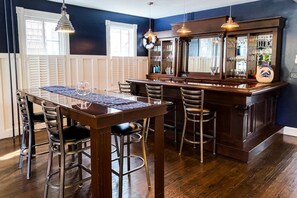 A bar area with a wooden bar counter, multiple stools, and pendant lighting. - Prime Location! Modern Comfort 1 Block to Gate 1 w/ Parking & Walkability (Annapolis)
