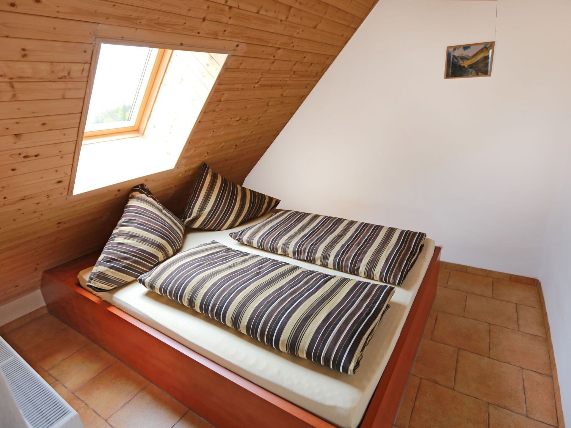A loft-style bedroom with a sloped ceiling, a skylight, and a bed with striped bedding.