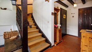 Eine Holztreppe mit Handlauf, ein kleiner Holzschrank mit Blumenvase und eine Tür mit Schlüsselloch und einem Schild.