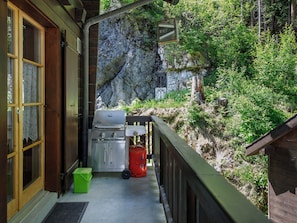 Un balcon avec un barbecue, une glacière verte et une bouteille de propane rouge.