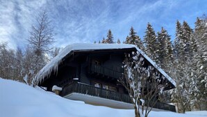 Eine Chalet mit Balkon, umgeben von schneebedeckten Bäumen und blauem Himmel.