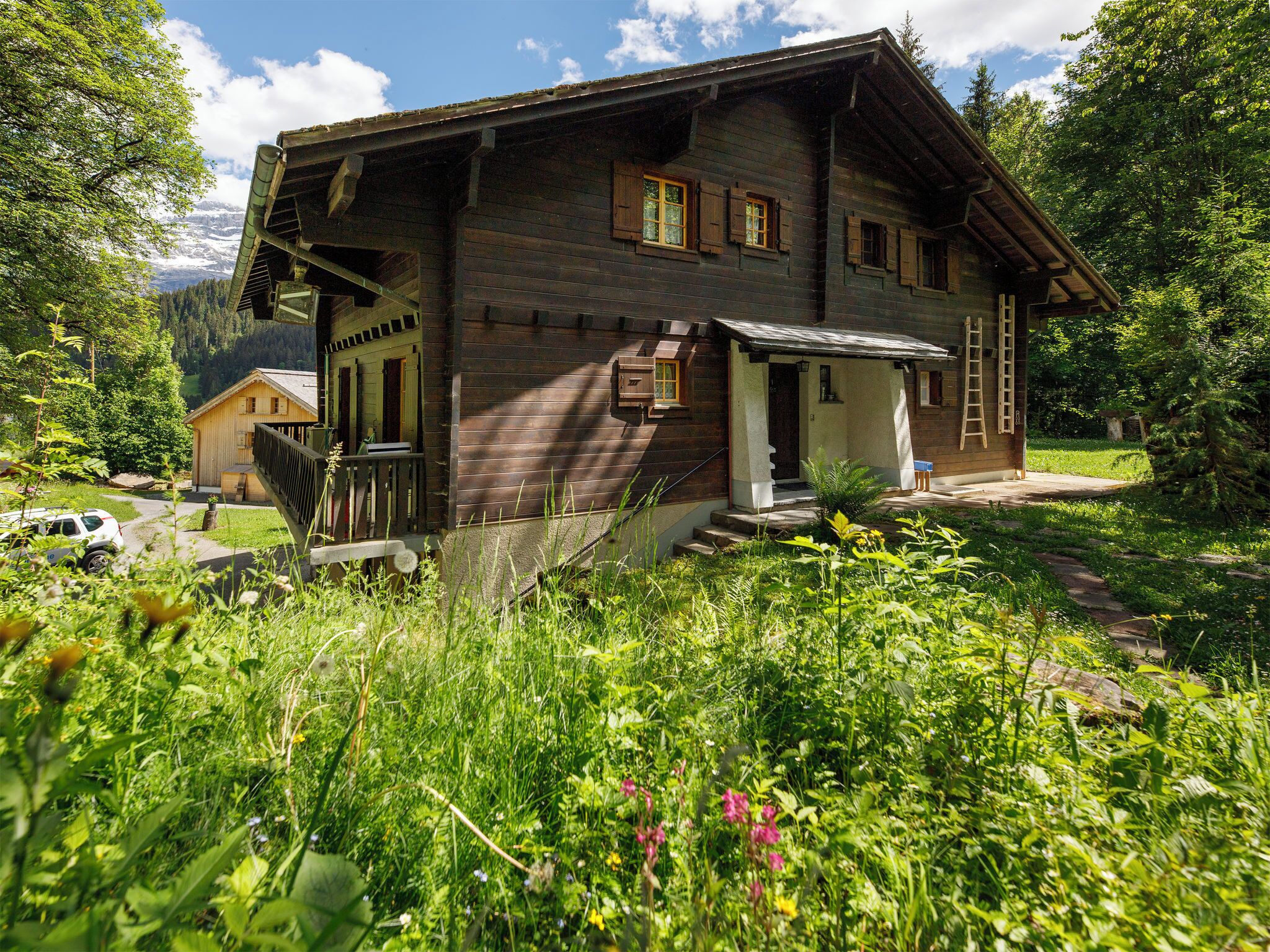 A wooden chalet with a porch, a staircase, and a view of a mountainous landscape.
