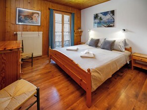 Ein Zimmer mit Holzwandverkleidung, das ein Bett, ein Sessel, ein Schreibtisch und ein Fenster mit Vorhängen bietet.