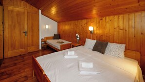 Ein Zimmer mit Holzwandverkleidung, einem großen Bett, einem kleineren Bett und einem Nachttisch mit Lampe.