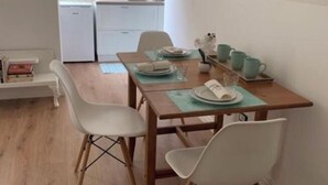 Un espace repas avec une table en bois, des chaises blanches et une cuisine en arrière-plan.