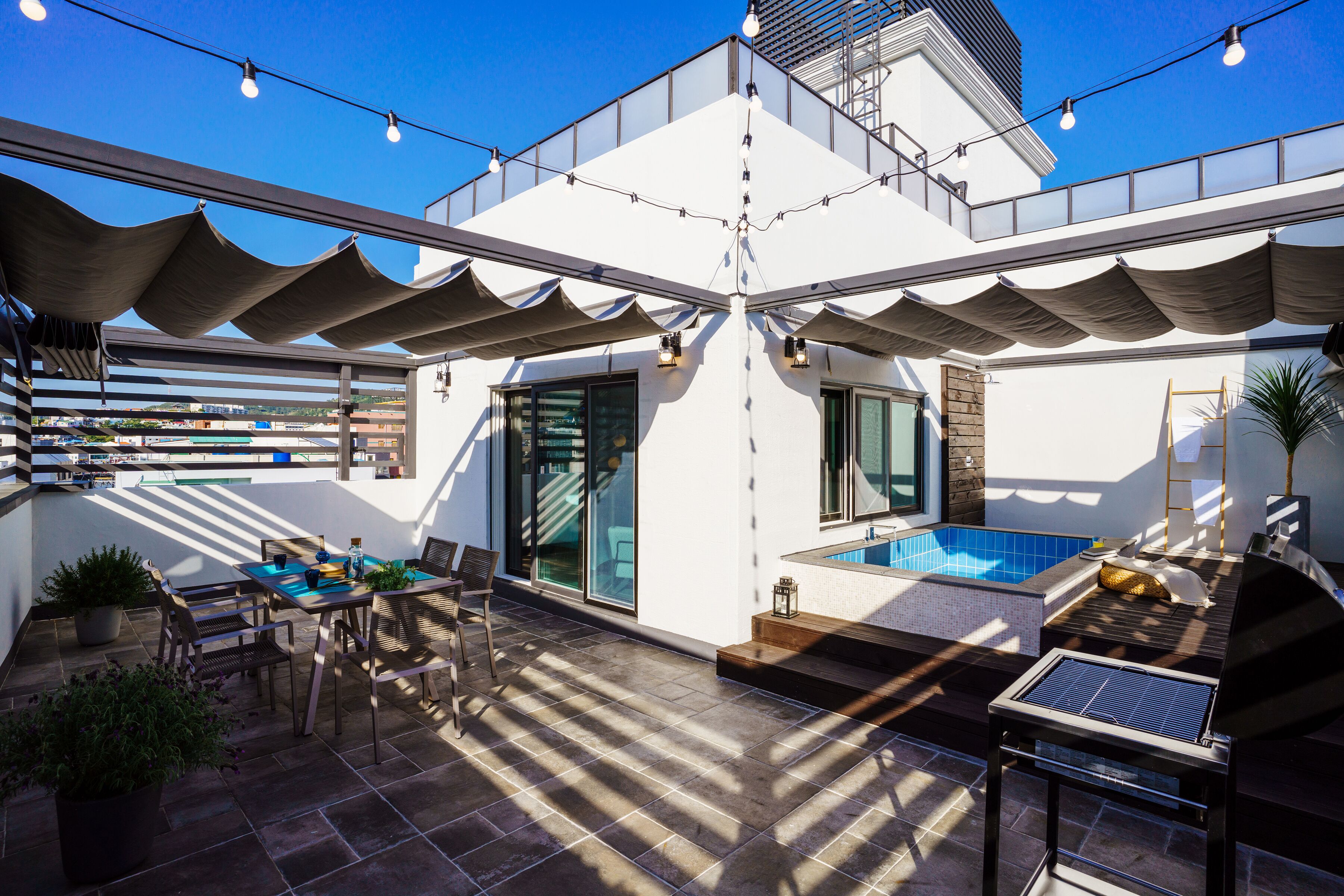 A rooftop patio with a pool, outdoor seating, and string lights.