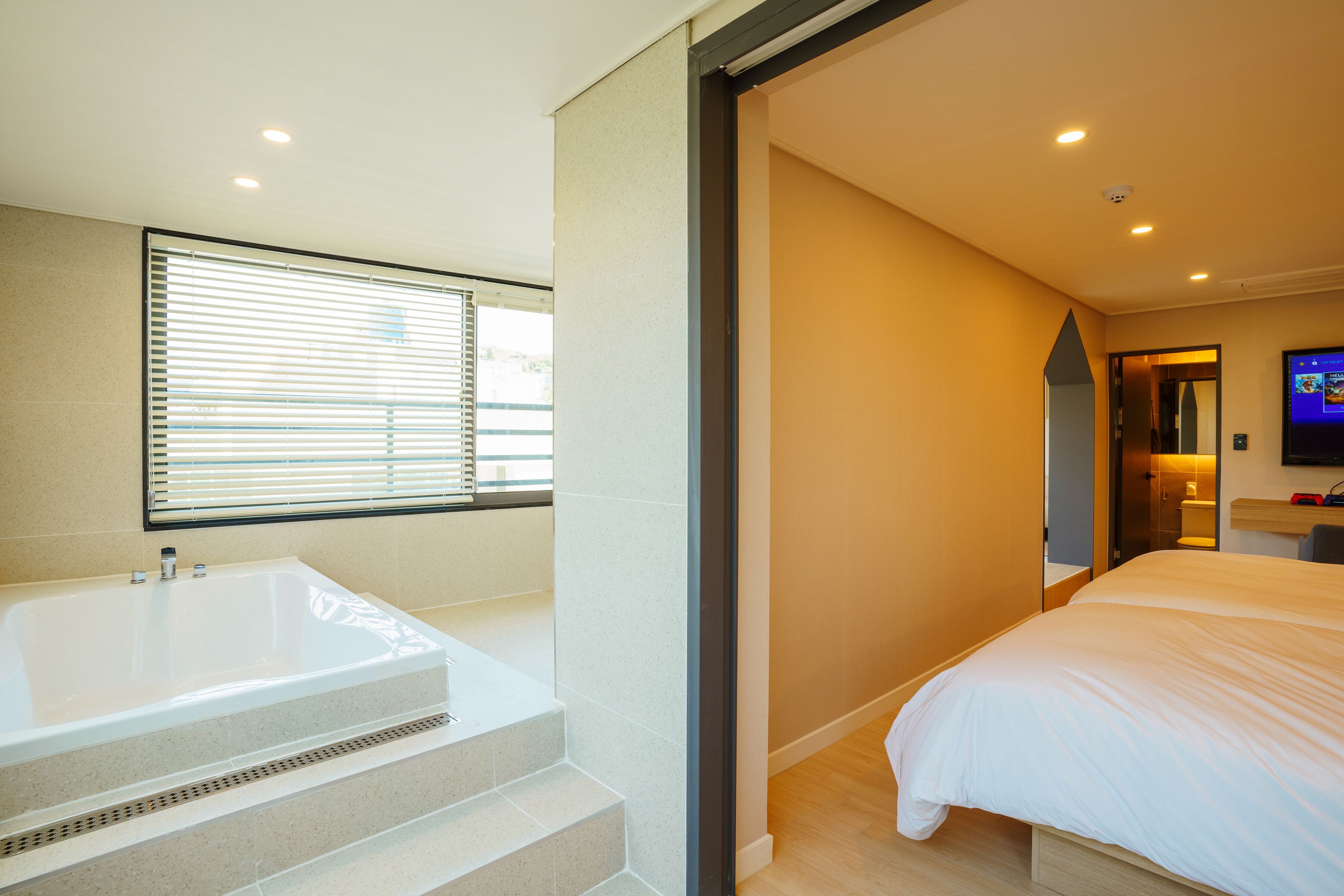 A modern hotel room with a large bed, a separate bathroom with a bathtub, and a television mounted on the wall.