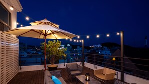 A rooftop terrace with outdoor seating, a large umbrella, string lights, and a view of the cityscape at night. - Hotel Pico (Tongyeong)