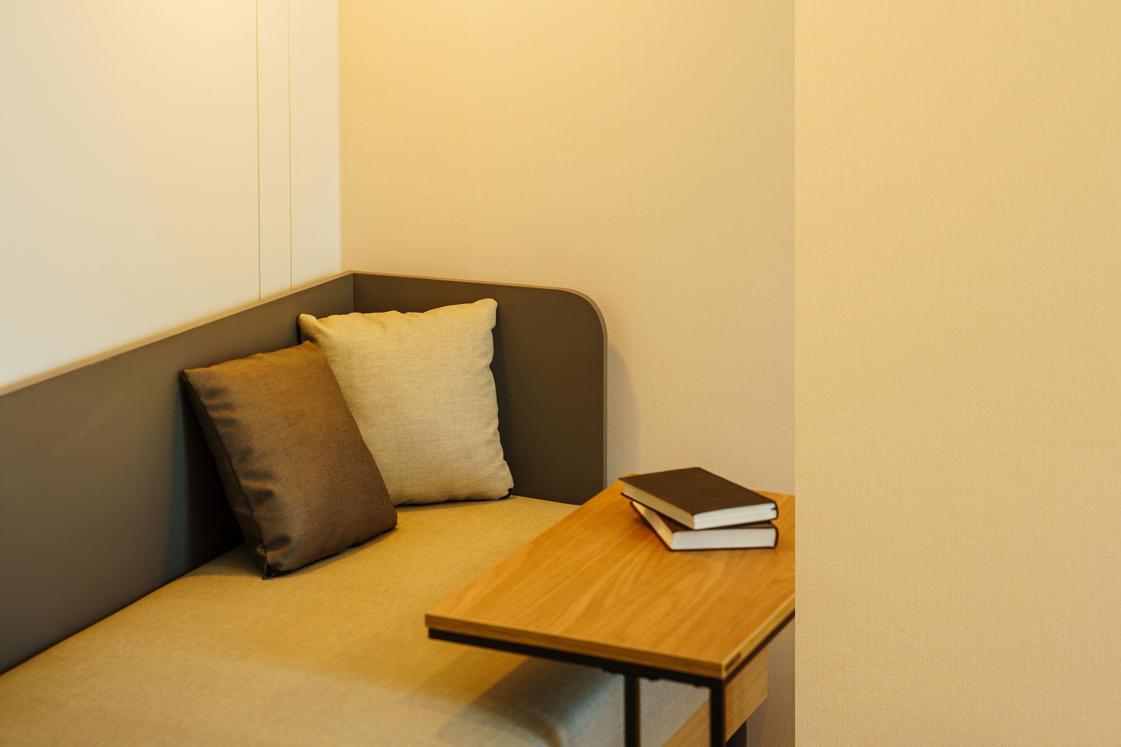Habitación de esquina con sofá, dos almohadas y una pequeña mesa de madera con un libro.