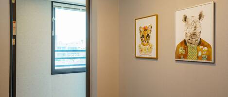 A hallway with two framed artworks on the wall, a window, and a door leading to another room.