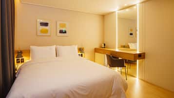 A hotel room with a large bed, a desk with a chair, a mirror, and artwork on the wall.