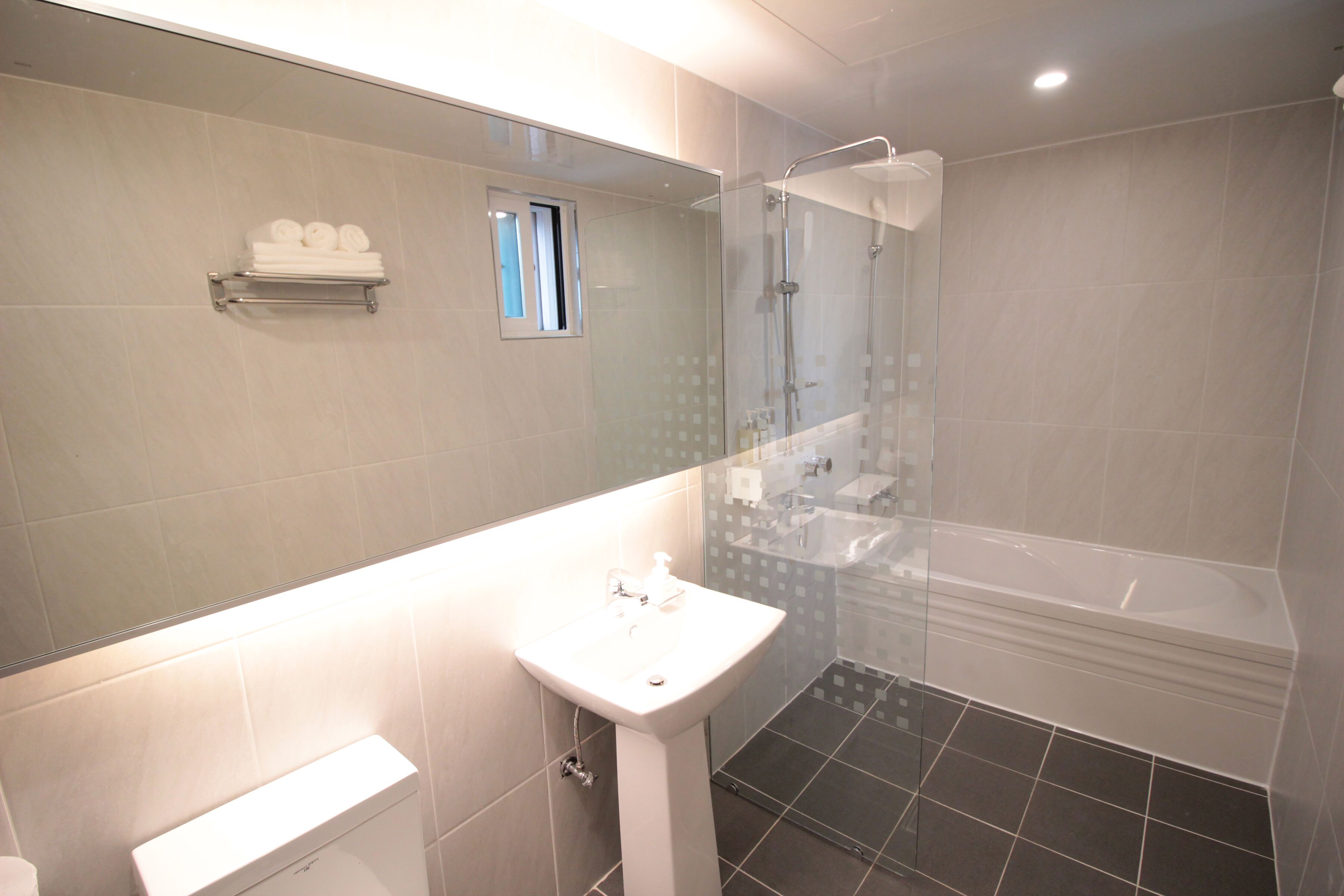 A modern bathroom with a glass-enclosed shower, a white pedestal sink, and a large mirror above the sink.
