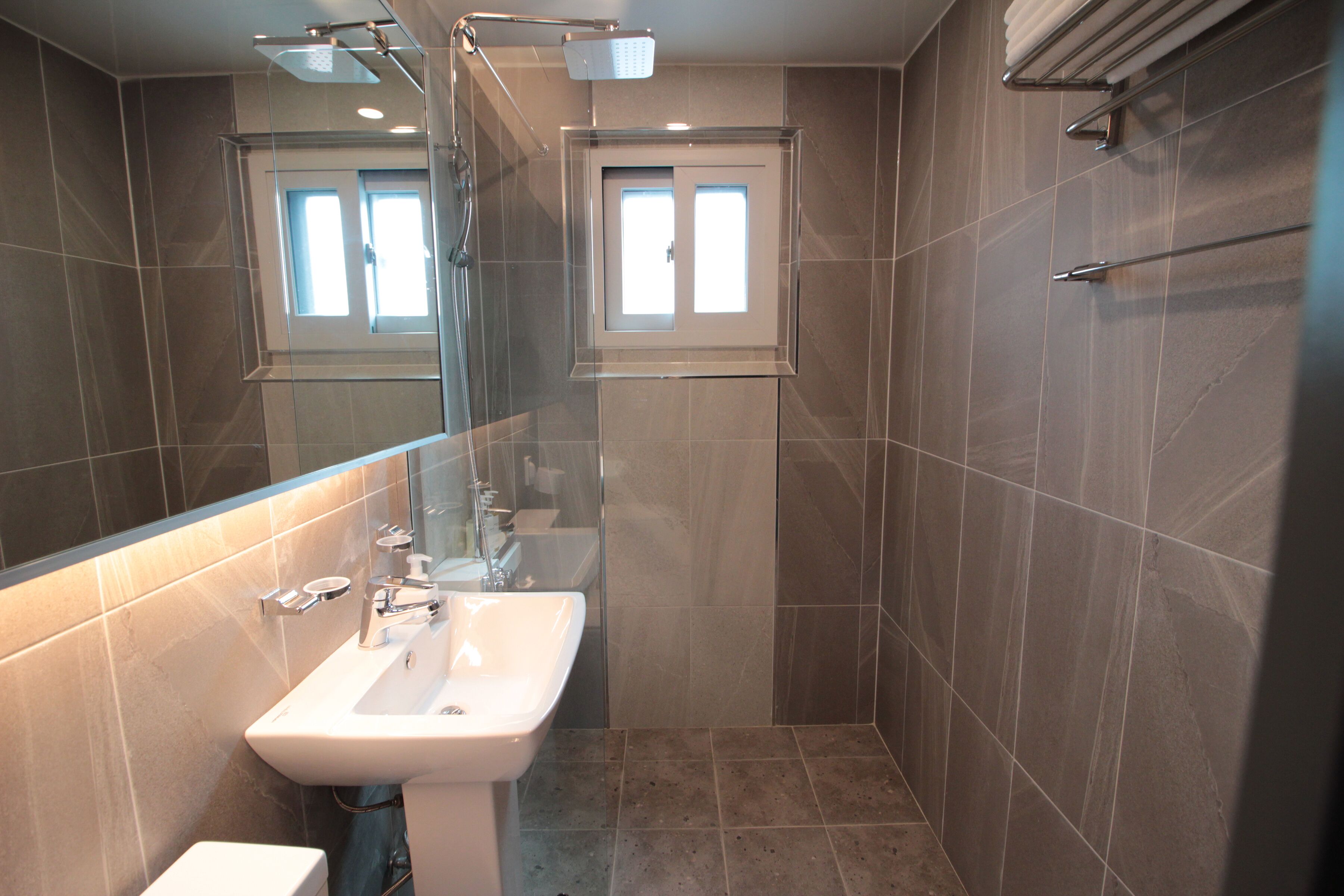 A modern bathroom with a glass-enclosed shower, a white sink, and a towel rack.