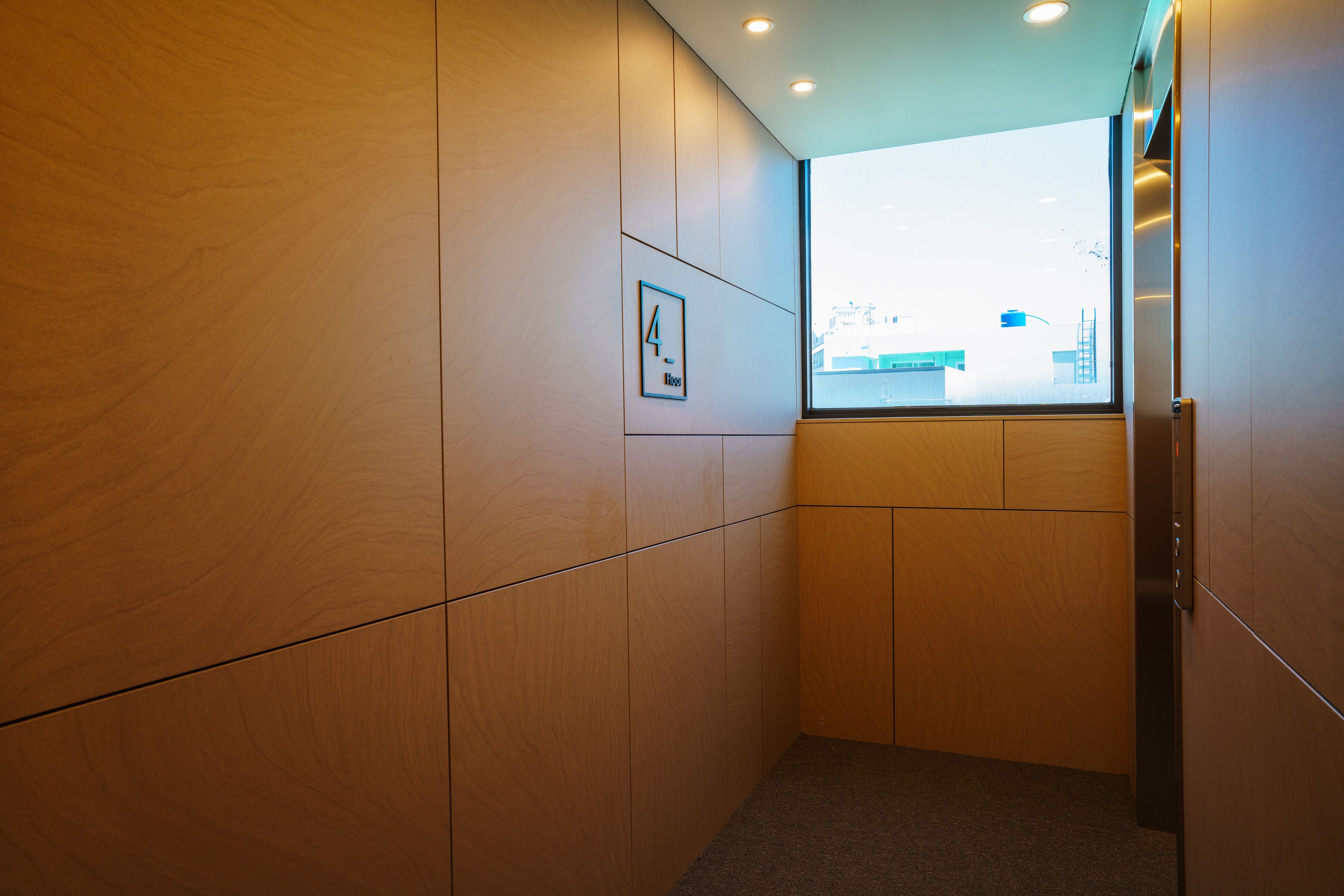 A modern interior with wooden paneling, a framed picture, and a window with a view of buildings.