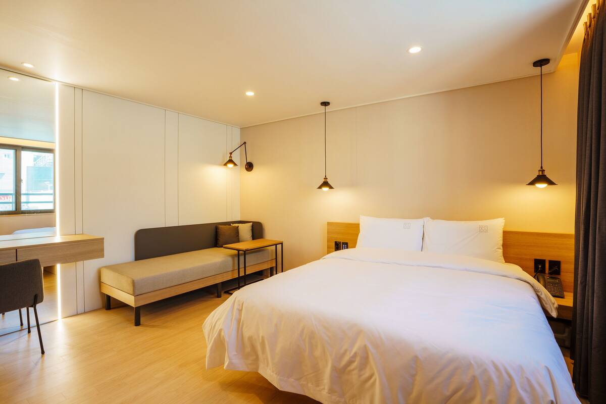 Moderni hotellihuone, jossa on suuri sänky, työpöytä, sohva ja kaksi riippuvalaisinta.