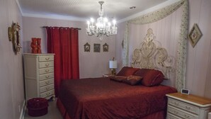 Ein Schlafzimmer mit einem großen Bett, einem Schminktisch, einem Nachttisch, einer Kristallleuchtre und einem dekorativen Kopfteil.